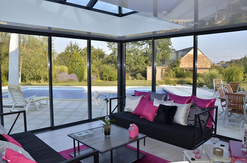 Intérieur d’une véranda aménagée en salon, vue sur la piscine